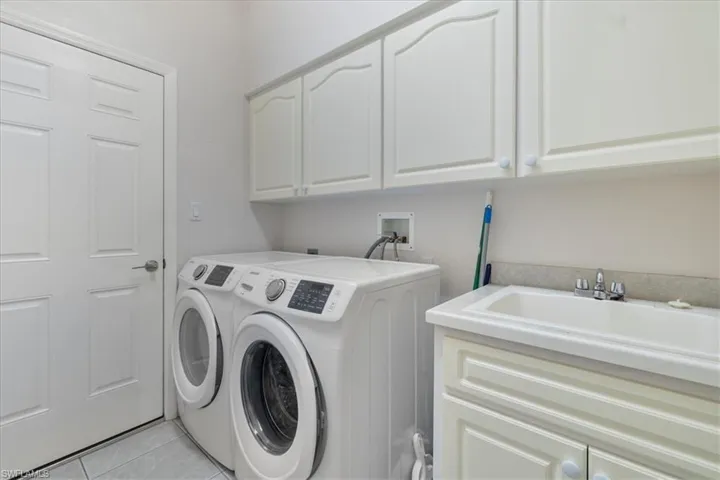 Washroom featuring independent washer and dryer, cabinets, sink, and light tile patterned floors