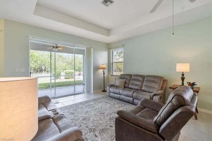 Living room with light tile patterned floors, a raised ceiling, and ceiling fan
