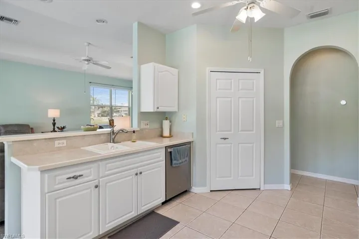 Kitchen with sink, white cabinets, stainless steel dishwasher, light tile patterned floors, and kitchen peninsula