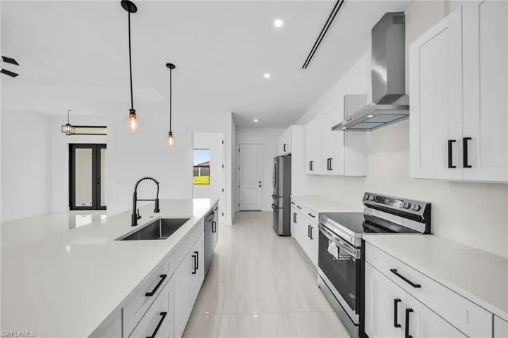 Kitchen with stainless steel appliances, wall chimney exhaust hood, white cabinetry, light countertops, and pendant lighting