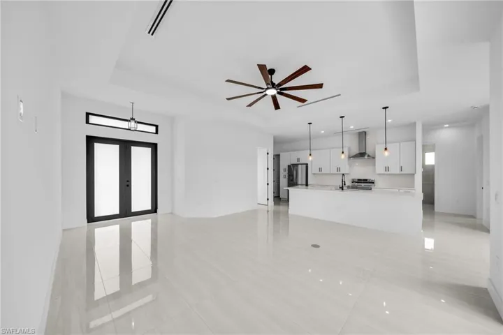 Unfurnished living room with a raised ceiling, french doors, a ceiling fan, and light tile patterned floors
