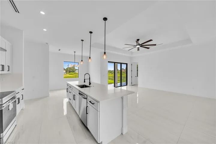 Kitchen featuring appliances with stainless steel finishes, a ceiling fan, a tray ceiling, an island with sink, and light countertops
