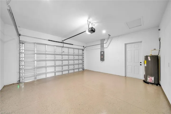 Garage with electric water heater, electric panel, and a garage door opener