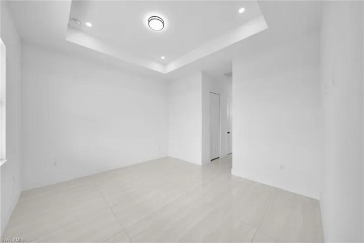 Empty room featuring a tray ceiling, recessed lighting, and light tile patterned floors
