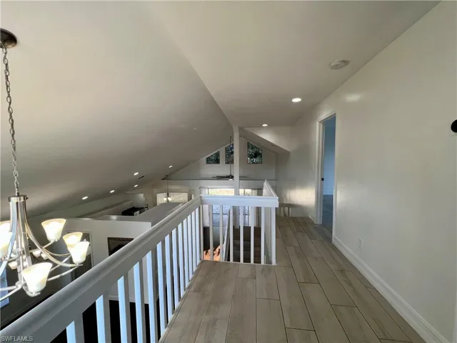 Hall with wood tiled floors, lofted ceiling, an upstairs landing, and suspended lighting