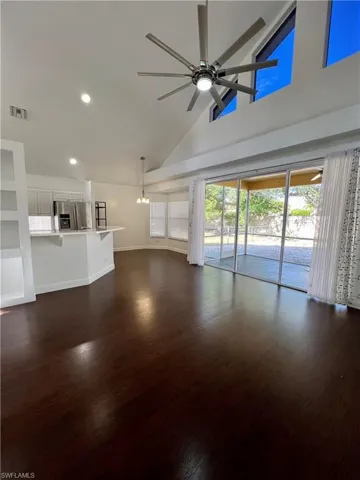Unfurnished living room featuring a ceiling fan, dark wood-style flooring, a chandelier, and vaulted ceiling