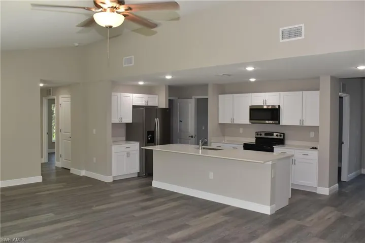Kitchen with white cabinets, appliances with stainless steel finishes, a center island with sink, and sink