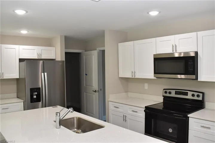 Kitchen featuring white cabinetry, sink, stainless steel appliances, and light stone counters
