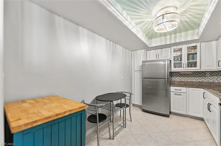 Kitchen with freestanding refrigerator, glass insert cabinets, a tray ceiling, white cabinetry, and backsplash