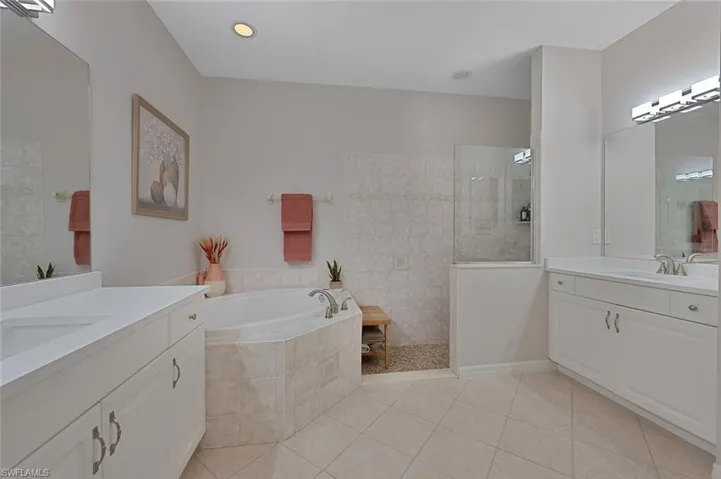 Bathroom featuring two vanities, a garden tub, walk in shower, and light tile patterned flooring
