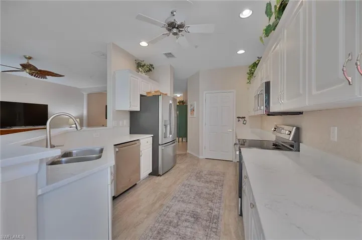 Kitchen featuring a ceiling fan, white cabinetry, stainless steel appliances, light stone countertops, and a peninsula