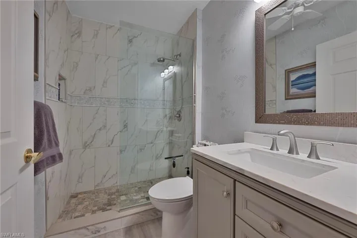 Bathroom featuring vanity, a marble finish shower, ceiling fan, and wallpapered walls