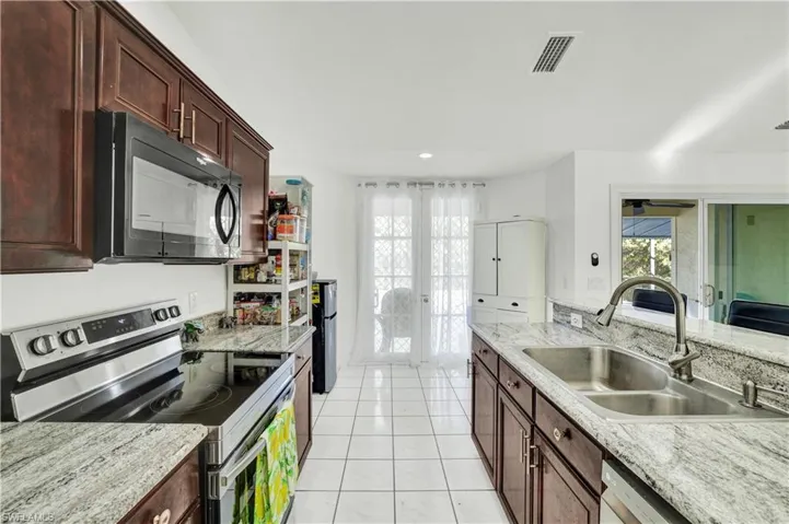 Kitchen featuring stainless steel appliances, dark wood finish cabinetry, light stone counters, light tile patterned floors, and recessed lighting