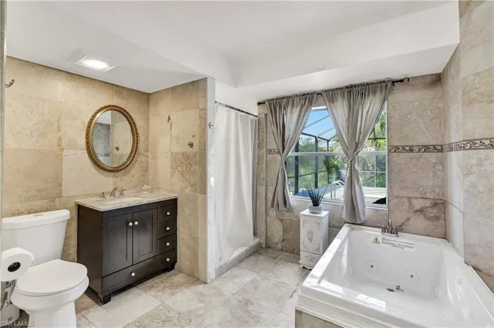 Full bathroom featuring tile walls, vanity, a shower stall, and a tub with jets