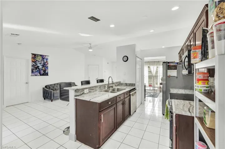 Kitchen featuring a breakfast bar, light tile patterned floors, a peninsula, dark wood finish cabinets, and a ceiling fan