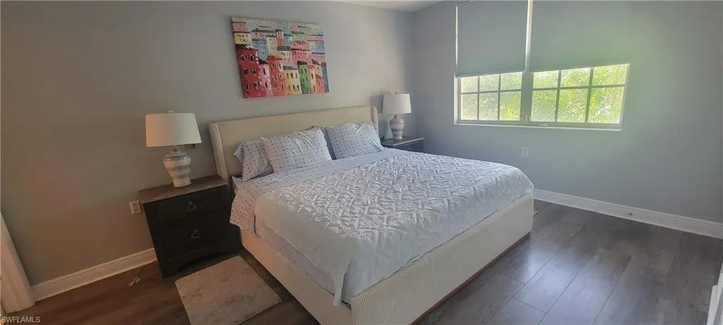 Bedroom featuring wood-finish flooring, neutral wall tones, and a window with roller shade