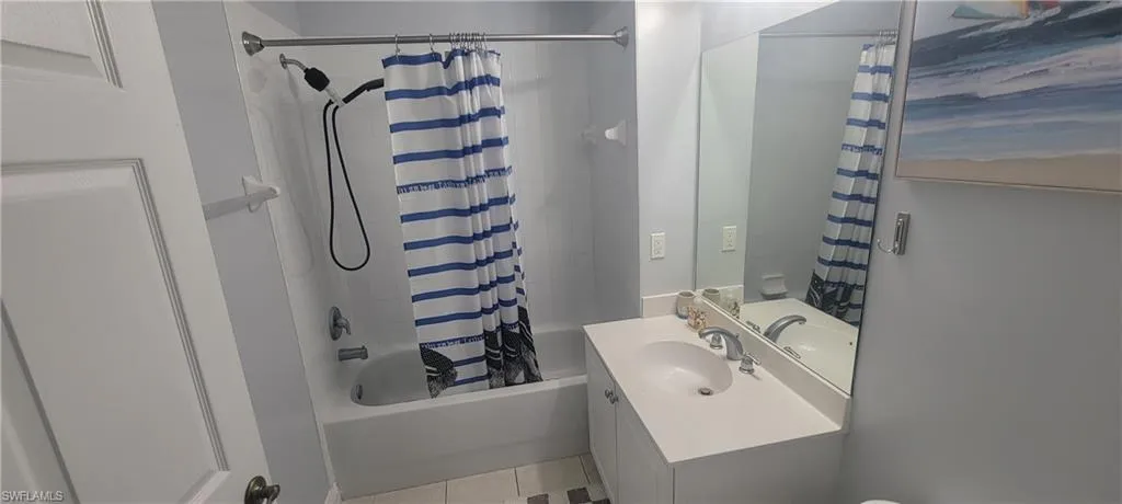 Bathroom featuring a white vanity with an integrated sink, a large mirror, and a tub-shower combination with a chrome shower rod