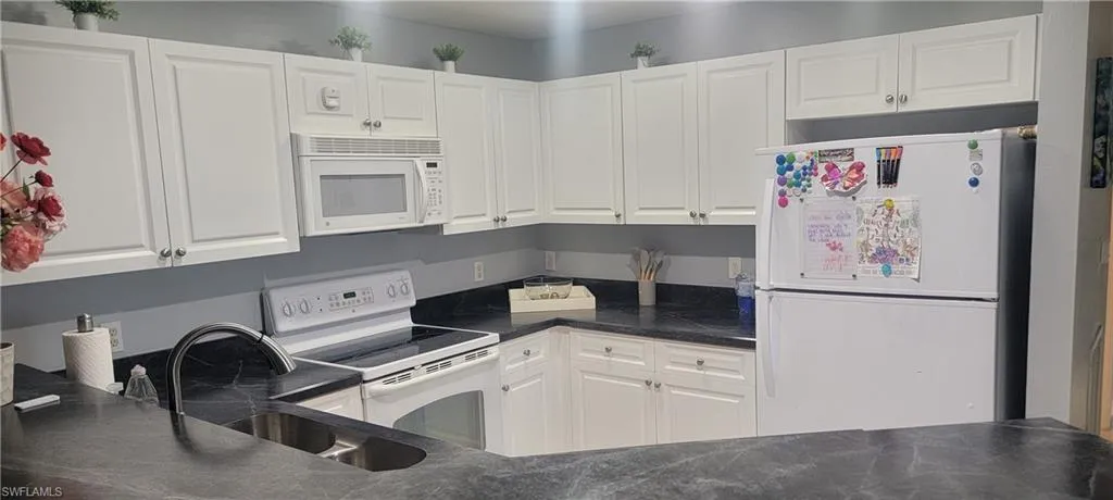 Kitchen featuring white cabinetry, dark countertops, a built-in microwave, and a stainless steel sink with a gooseneck faucet