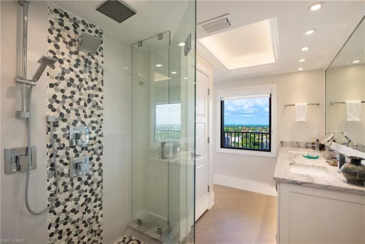 Full bathroom featuring a deluxe shower stall, a raised ceiling, double vanity, wood finished floors, and recessed lighting
