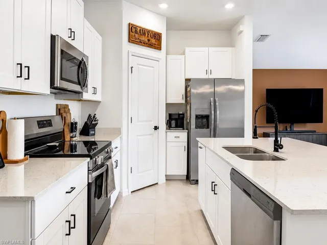 Modern kitchen featuring white cabinetry with matte black hardware, stainless steel appliances, solid surface countertops, a double basin sink with a black pull-down faucet, and light-colored tile flooring