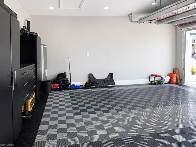Garage interior featuring checkerboard pattern flooring, light gray walls, built-in black cabinetry with silver-tone hardware, recessed ceiling lighting, and a visible garage door mechanism