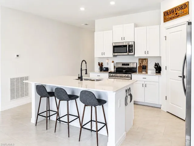 Modern kitchen featuring a central island with integrated sink, stainless steel appliances, white cabinetry, recessed lighting, and light-toned tile flooring