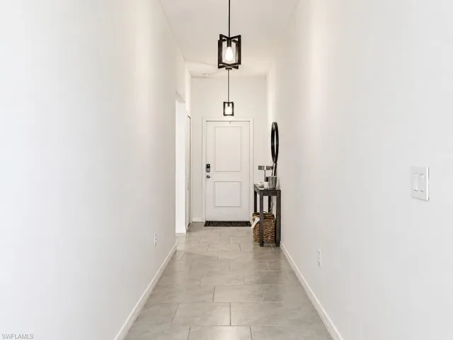 Hallway featuring tile flooring, white walls, two contemporary pendant light fixtures, and a white paneled door with dark hardware