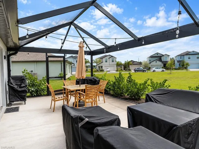 Screened patio with string lighting, concrete flooring, and a landscaped perimeter