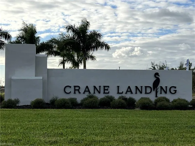 Community entrance monument featuring a white stucco finish and raised black lettering, surrounded by manicured green lawn and tropical plantings