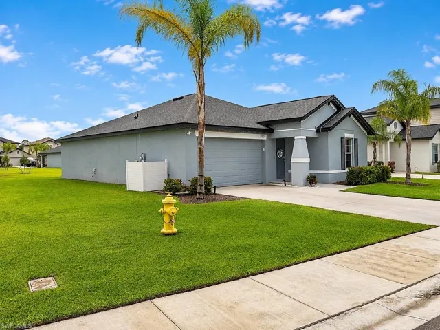 Exterior featuring a light grey stucco finish, dark grey roofing, and a prominent palm tree