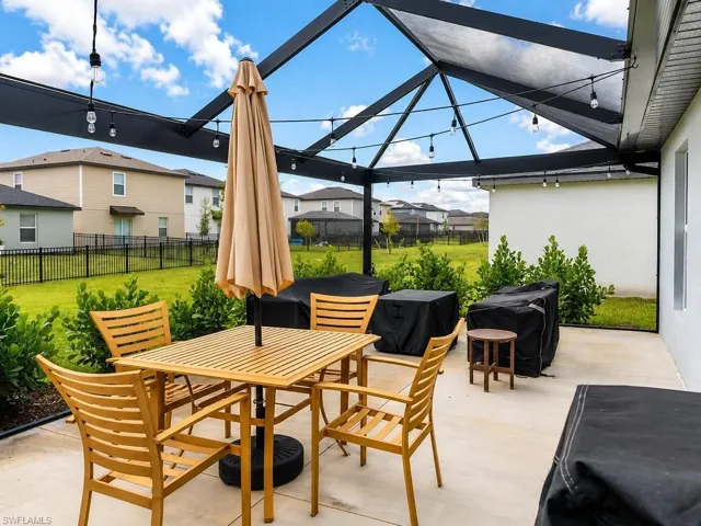 Spacious concrete patio featuring a black metal pergola with string lighting and a partial shade cover