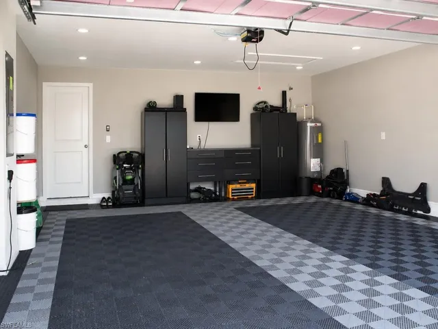Attached garage featuring checkerboard interlocking floor tiles, recessed lighting, a white pedestrian door, and a water heater