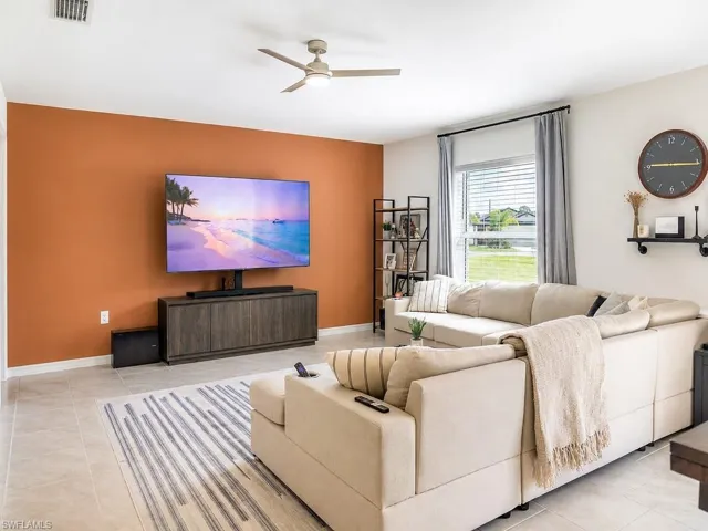 Spacious living area featuring neutral tile flooring, a contemporary ceiling fan, and ample natural light from a large window with blinds and drapes
