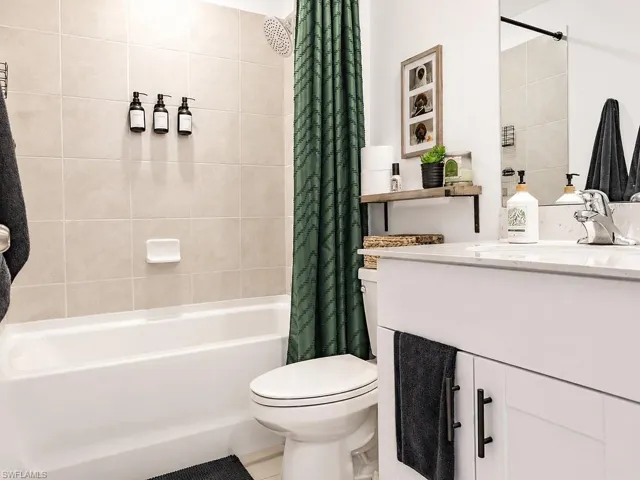 Bathroom featuring a white vanity with a light-toned countertop, a shower-tub combination with light-toned tile surround, a built-in shower head, and a wall-mounted shelving unit