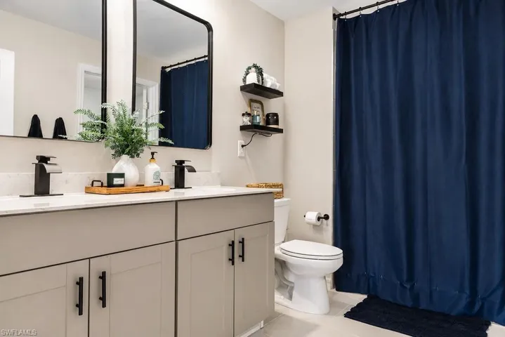 Bathroom featuring a double vanity with light gray cabinetry, matte black hardware, and an expansive countertop