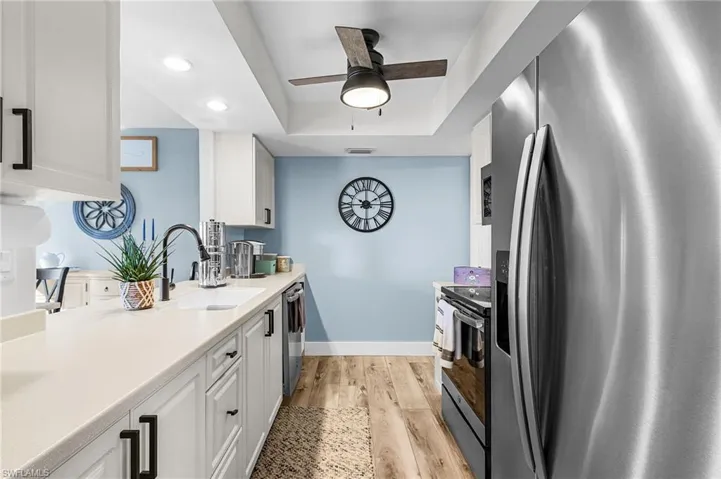 Kitchen featuring stainless steel appliances, white cabinetry, recessed lighting, a raised ceiling, and light wood-type flooring