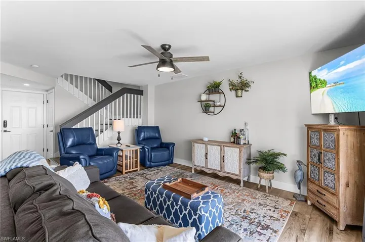 Living area with wood finished floors, ceiling fan, and stairs