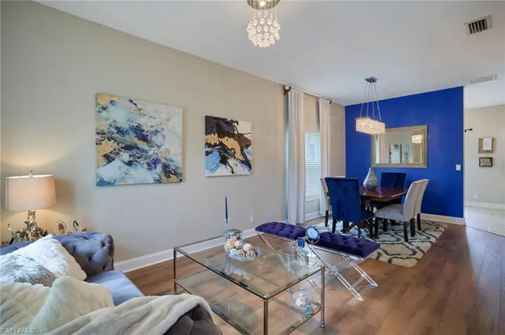Open-concept living space featuring wood-finish flooring, a contemporary chandelier, and a dining area with a statement accent wall