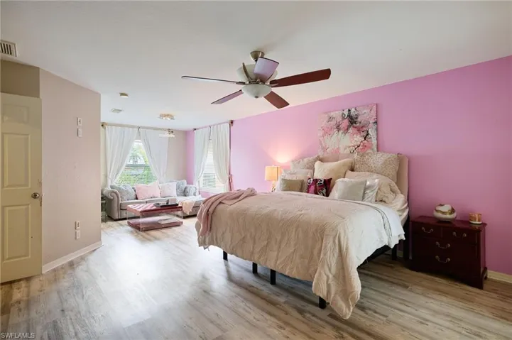 Open-concept room featuring wood-finish flooring, a ceiling fan with integrated lighting, and multiple windows with vertical blinds