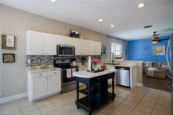 Open-concept kitchen featuring white cabinetry, stainless steel appliances, a tile backsplash, and a movable kitchen island