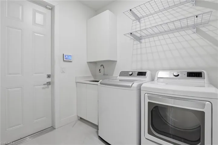 Dedicated laundry space featuring a utility sink, white cabinetry, and built-in wire shelving
