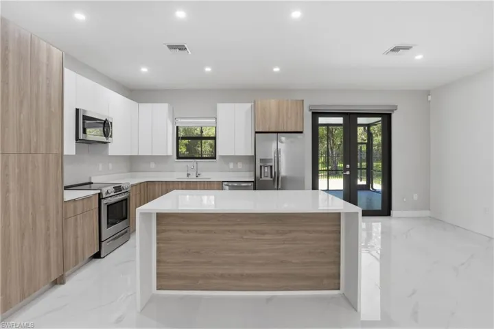Contemporary kitchen featuring wood-finish and white cabinetry, stainless steel appliances, a center island with a light-toned countertop, and recessed lighting