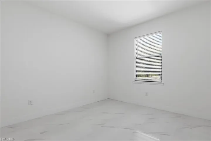 Room featuring a single window with blinds, white walls, white baseboards, and light-colored tile flooring with subtle veining