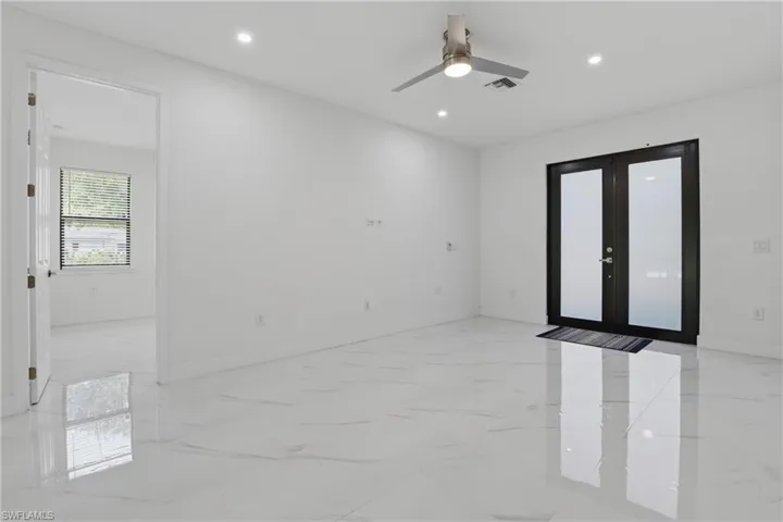 Spacious room featuring glossy white tile flooring, a contemporary ceiling fan with integrated lighting, recessed ceiling lights, and double French doors with frosted glass panels
