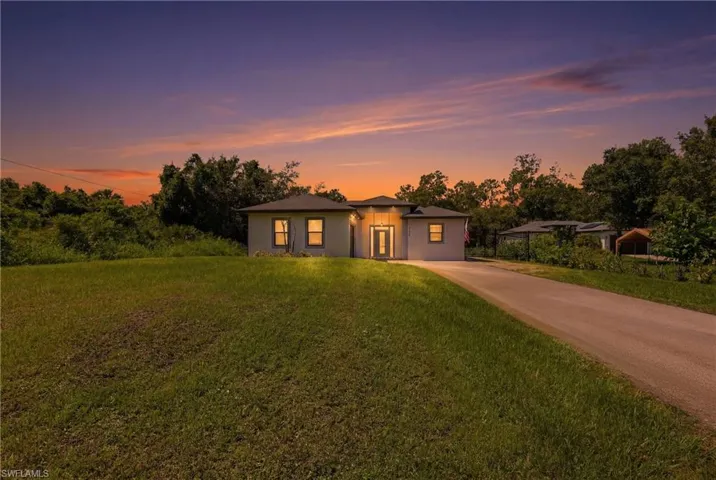 Modern ranch-style home featuring a light-toned exterior, dark roof, and a prominent front entry with vertical window accents