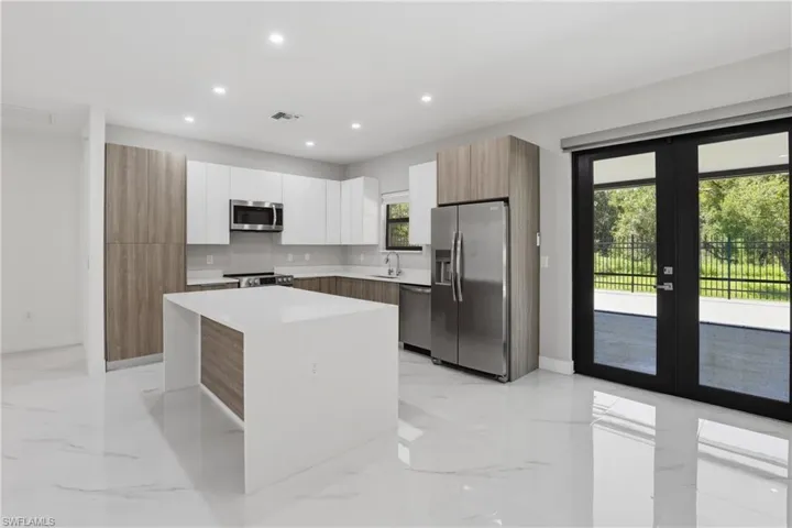 Modern kitchen featuring white and wood-finish cabinetry, a large center island with a white countertop, stainless steel appliances, and polished tile flooring