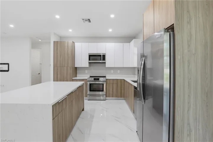 Contemporary kitchen featuring an expansive island with a white countertop, two-tone cabinetry, stainless steel appliances, recessed lighting, and large format floor tiling