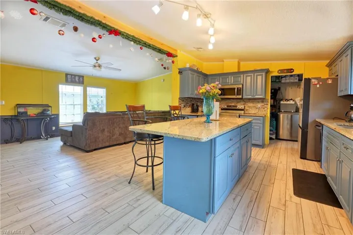Kitchen featuring a kitchen island, appliances with stainless steel finishes, decorative backsplash, light hardwood / wood-style floors, and light stone counters