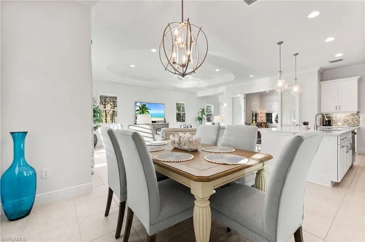 Dining space featuring light tile patterned floors, an inviting chandelier, a tray ceiling, recessed lighting, and crown molding