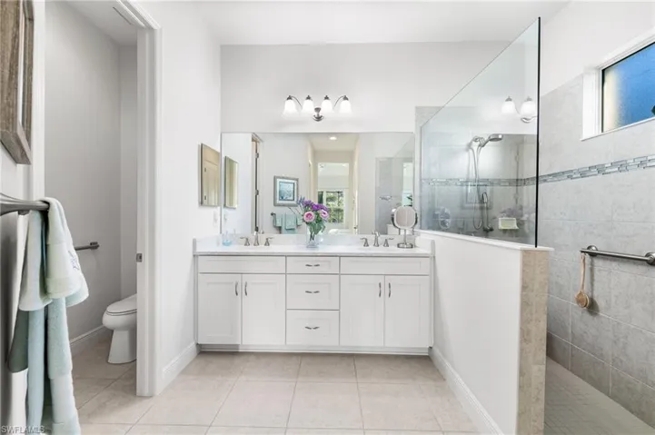 Bathroom with tile patterned floors, toilet, a sink, double vanity, and walk in shower